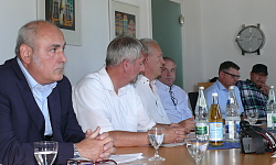 An einem großen Tisch im Sitzungssaal sitzen Teilnehmer und Pressevertreter. 