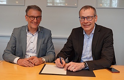 Bernhard Palm unterschreibt einen Vertrag, Markus Ibert sitzt neben ihm