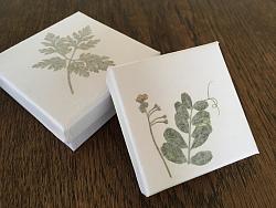 Das Bild zeigt zwei weiße Schachtenln. Auf dem Deckel sind grüne Blumen eingearbeitet. 