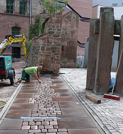 Der Platz vor dem Stadtmuseum Tonofenfabrik wird umgestaltet. In Verlängerung der Stadtmauer zeigt das Pflaster den Verlauf der Mauer. Ein Bauarbeiter verlegt die letzten Steine Pflaster. 