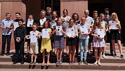 Die Preisträger gruppieren sich auf einer Sandsteintreppe. Jeder hält stolz seine Urkunde in die Kamera und lächelt. 