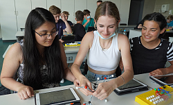 Drei Mädchen sitzen vor einem chemischen Modell, alle drei haben ein Tablett vor sich liegen. 