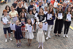 Preisträgerinnen und Preisträger der Musikmedaille 2022 stehen mit Urkunde und Medialle auf dem Marktplatz und lächeln. 