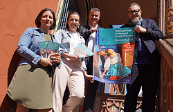 Die vier Personen stehen auf der Treppe und halten das Kulturprogramm und das Plakat in den Händen. 