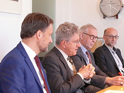Markus Ibert, Oberbürgermeister Dr. Wolfgang G. Müller, Dr. Bernd Dallmann und Arnfried Sieckinger sitzen von links nebeneinander an einem Besprechungstisch. Alle sind mit Anzug und Kravatte gekleidt. OB Müller gestikuliert und erklärt. 