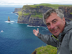 Andreas Eller deutet auf die irländischen Klippen und das Meer hinter ihm ihm Bild.