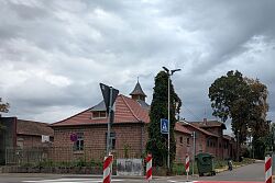Straßenkreuzung mit rotem Radweg, mehreren Verkehrszeichen und Backsteingebäuden im Hintergrund.