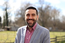 Das Foto zeigt einen Mann mit Bart, der im Grünen steht.