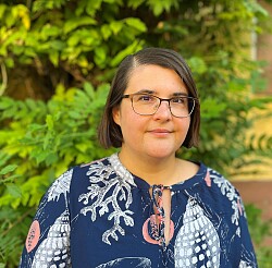 Portrait Frau mit kinnlangen braunen Haaren, Brille und mit blauer Bluse gekleidet.