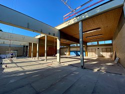 Die Fassade der Gymnasikhalle des Max-Planck-Gymnasiums wird im Zuge der Sanierung demontiert. Bei einem Teil der Halle fehlt das Dach, man sieht Eisenträger, Betonboden und blauen Himmel