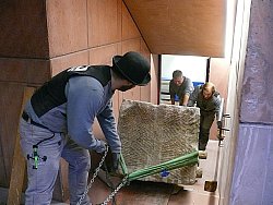 Auf dem Bild sieht man, wie drei Männer der Firma Nuvolin den Sarkophag über Holzplanken, die auf die treppenstufen gelegt wurden im Stadtmuseum Tonofenfabrik ins Untergeschoss transportieren.