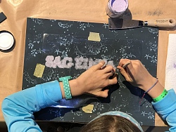 Ein Schild wird mithilfe von verschiedenen Farben und Materialien bearbeitet und verziert.