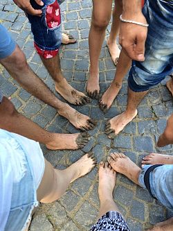 Das Foto zeigt mehrere nackte Beine mit hochgekrempleten oder kurzen Hosen und mit Schlamm verschmierte Füße, die im Kreis zusammenstehen.
