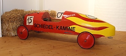 Zu sehen ist eine rote Seifenkiste - ein selbsgebauter Wagen mit vier Rändern und niedriger Karosserie aus einfachsten Materialien. Auf der Siefenkisten steht die Nummer 15. 