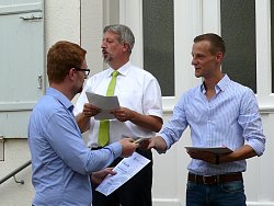 Martin Stehr überreicht einem Herrn in einem blauen Hemd eine Urkunde für die erfolgreiche Teilnahme am Stadtradeln 2018. Bürgermeister Tilman Petters steht daneben und liest aus einer Liste vor.