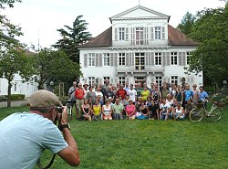 Zu sehen ist ein Gruppenbild von Teilnehmenden und Preisträgern des Stadtradelns zusammen mit Bürgermeister Tilman Petters und Martin Stehr vom Stadtplanungsamt. Alle haben sich vor dem Brunnen im Rathaus-Innehof aufgestellt, die erste Reihe sitzt im Gras, links und rechts von der Gruppe steht jeweils ein Fahrrad im Rasen. Links im Vordergrund steht ein Fotograf mit Schiebermütze, der gerade ein Bild von der Gruppe macht.