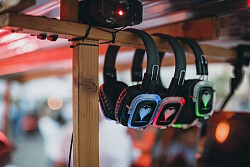Mehrere Silent-Disco-Kopfhörer hängen an einem Holzgestell, jeder mit unterschiedlich farbigen LED-Leuchten an den Ohrmuscheln.