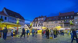 Menschen mit Kopfhörern tanzen vor blauem Abendhimmel auf dem Lahrer Marktplatz.