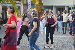 Auf dem Foto sind mehrere Gäste mit Kopfhörern zu sehen, die auf dem Markplatz tanzen 