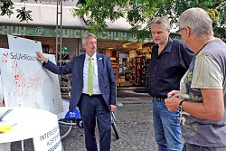 Im SoLAHRdachkataster können sich Lahrer Bürgerinnen und Bürger kostenfrei darüber informieren, ob ihr Dach für Solarenergie geeignet ist – denn Licht und Wärme liefert die Sonne gratis. Bürgermeister Tilman Petters steht neben einem Plakat in der Marktstraße und spricht mit zwei interessierten Bürgern.