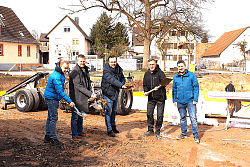 Fünf Menschen beim Spatenstich vor der Baustelle