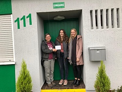 Das Foto zeigt drei junge Frauen. Es wird ein Scheck übergeben. 