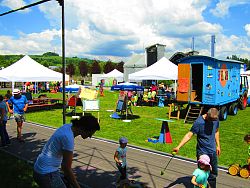 Das Bild zeigt einen Blick auf das Landesgartenschau-Gelände. Neben dem Spielmobil Traktor sind verschiedene Bastel- und Spielstationen aufgebaut und zahlreiche Kinder und ihre Eltern sind zwischen den Stationen unterwegs.