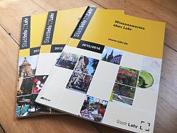 Drei gelbe StadtInfo Lahr Broschüren aus den vergangenen Jahren liegen fächerförmig ausgebreitet auf Holzdielen.