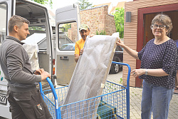 Vor einem weißem Kombi stehen zwei Mitarbeiter des BGL, vor sich einen Transportwagen, auf den sie ein hochformatiges Bild wuchten. Daneben steht Gabriele Bohnert, Leiterin des Museums, und beobachtet das Ganze lächelnd. 