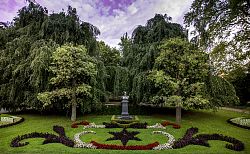 Zu sehen ist eine kunstvoll angelegte Blumenrabatte in weiß, rot und dunkelrot, am Fuße der Bismarck-Büste im Stadtpark Lahr. Dahinter mächtige, alte Bäume.