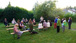 Oberbürgermeister Markus Ibert steht beim Bürgertreff im Burgheimer Kirchgarten unter einem Baum vor circa 20 Besucherinnen und Besuchern, die auf Bierbänken sitzen oder neben ihm stehen.