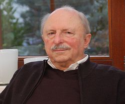 Porträt des Autors Stefan Pflaum. Er trägt einen schwarzen Pullover und eine schwarze Überziehweste. An seinem Hals blitzt ein weißes Hemd hervor. Stefan Pflum trägt einen grauen Schnauzbart und eine Halbglatze mit grauen Haaren.