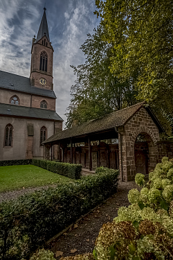 Blick aus dem Kirchhof auf den Turm der Stiftskirche. Rechts die Grabanlagen. Der Himmel ist verdunkelt als kommt gleich ein Gewitter.