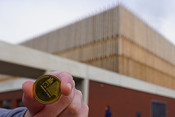 Jemand hält eine Stadt Gulden Lahr Münze in die Kamera, im Hintergrund ist etwas verschwommen die Mehrzweckhalle zu sehen.