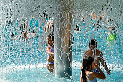 Kinder spielen im Wasser unter einem Wasserfall im Terrassenbad an einem sonnigen Tag