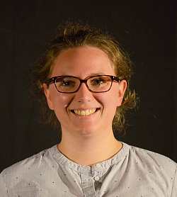 Portraitfoto einer jungen Frau mit Brille, die in die Kamera lächelt.
