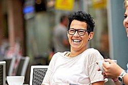 Zwei Frauen sitzen lachend in einem Straßencafé, eine hält eine Tasse in ihrer Hand.