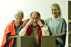 Das Foto zeigt drei Peronen, die zusammen stehen. Auf der linken Steite steht Gisela Griesbaum. Sie trägt kurze graue Haare und eine Brille. Um ihre Schultern liegt ein orangefarbener Pullover. Darunter trägt sie eine blaugeblümte Bluse. Ihre linke Hand liegt auf der rechten Schulter von Bruno Thost. Bruno Thost trägt graue Haare, die aus dem Gesicht gekämmt sind. Sein grauer Vollbart ist kurzgeschnitten. Seine Ellenbogen sind aufgestützt und er stützt seinen Kopf auf seine Fäuste. Auch er trägt einen roten Pullover um seine Schultern. Neben ihm steht Verena Rohkohl. Sie trägt ihre langen, blonden Haare zu einem Pferdeschwanz gebunden. Ihre rechte Hand liegt auf der linken Schulter von Bruno Thost. Sie trägt einen hallblauen Pullover. Darunter blitzt ein weißes T-Shirt am Kragen hervor. Alle drei Personen lächeln freundlich in die Kamera.