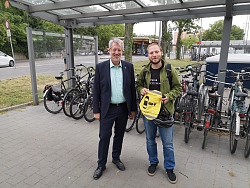 Lahrs Baubürgermeister Tilman Petters überreicht einen Rücksacküberzieher, bedruckt mit dem Hinweis zum Überholabstand, an Egor Gordeev (von links).