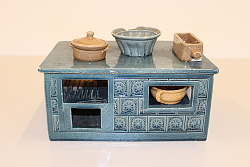 Es ist ein Puppenherd aus Ton abgebildet, auf dem kleine Gefäße stehen.