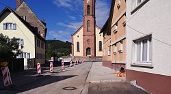 Von Häusern gesäumte Straße in Sulz, in der Bauarbeiten stattfinden, links stehen rot-weiße Warnbaken, man blickt direkt auf die Kirche