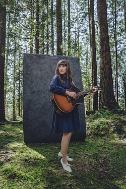 Frau mit Gitarre vor einem Stein im Wald