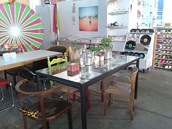 Die VHS Lahr bietet neue Kursangebote. Das Bild zeigt einen Blick in die Smyle Art Lounge von Simone Müller. Im Vordergrund steht ein Glastisch mit Kerzenhaltern aus Holzklötzen und Kräutern in Sektkübeln. Verschieden Stühle stehen um den Tisch. Im Hintergrund sind einige Kunstwerke zu sehen. 