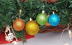 Vier bunte Weihnachtskugeln an einem Tannengesteck.