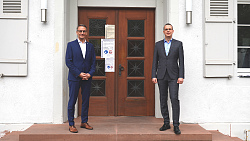 Das Foto zeigt zwei Männer im Anzug vor einer großen Tür.