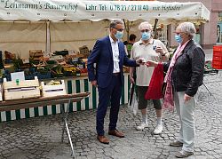 Oberbürgermeister Markus Ibert überreicht einem älteren Ehepaar ein Willkommensgeschenk auf dem Lahrer Wochenmarkt.