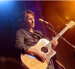 Auf dem Foto ist Steven Bailey mit einer Gitarre auf der Bühne zu sehen 