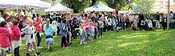 Das Bild zeigt eine große Zahl von Gästen des Wohngebietsfestes im Kanadaring. Es sind Erwachsenen und Kinder unterschiedlichen Alters, die auf grünem Rasen stehen. MAnche Kinder tanzen. Im Hintergrund sieht man weiße Zeltdächer, die über verschiedenen Ständen aufgebaut sind.