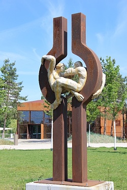 Skulptur aus Cortenstahl und Keramik: Zwei Personen sitzen in bauchigen Ausbuchtungen zwischen Stahlpfosten.
