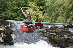 Das Bild zeigt zwei Jungen, die bei der Kanu-Freizeit des Kinder- und Jugendbüros im Kanu ein Gefälle hinunterfahren.